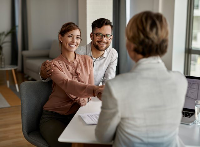 Young happy couple shaking hands with insurance agent during a meeting in the office.